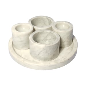 Puede incluir: Un juego de cuatro candelabros de mármol blanco con una bandeja de mármol blanco a juego. Los candelabros son cilíndricos y tienen un acabado liso y pulido.