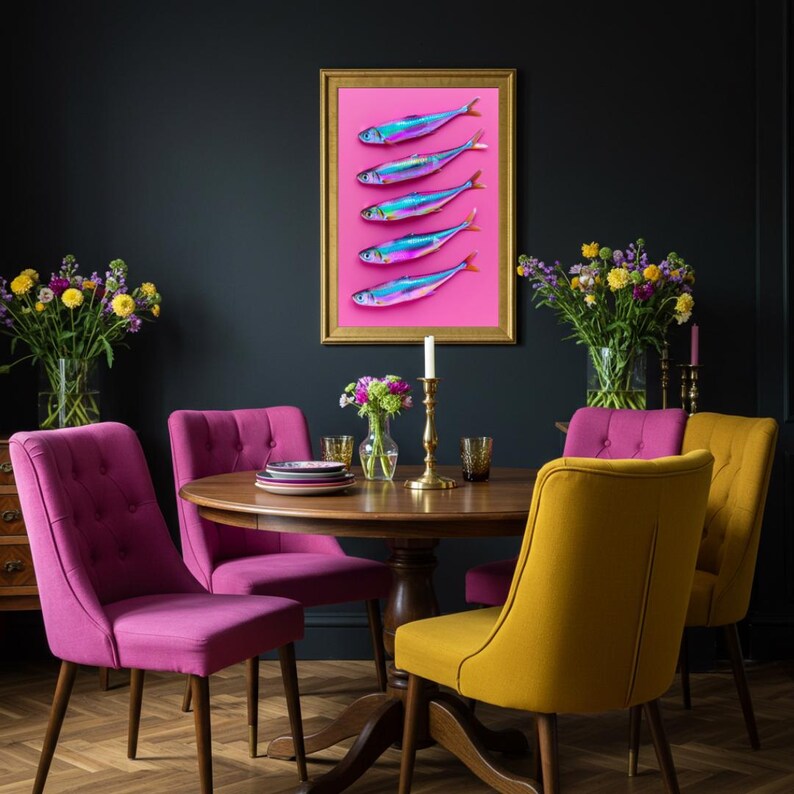 May include: A dining room scene featuring a round wooden table surrounded by upholstered chairs in shades of pink and yellow. A framed artwork with colorful fish art hangs on the dark wall. Vases of flowers and a candle holder complete the decor.