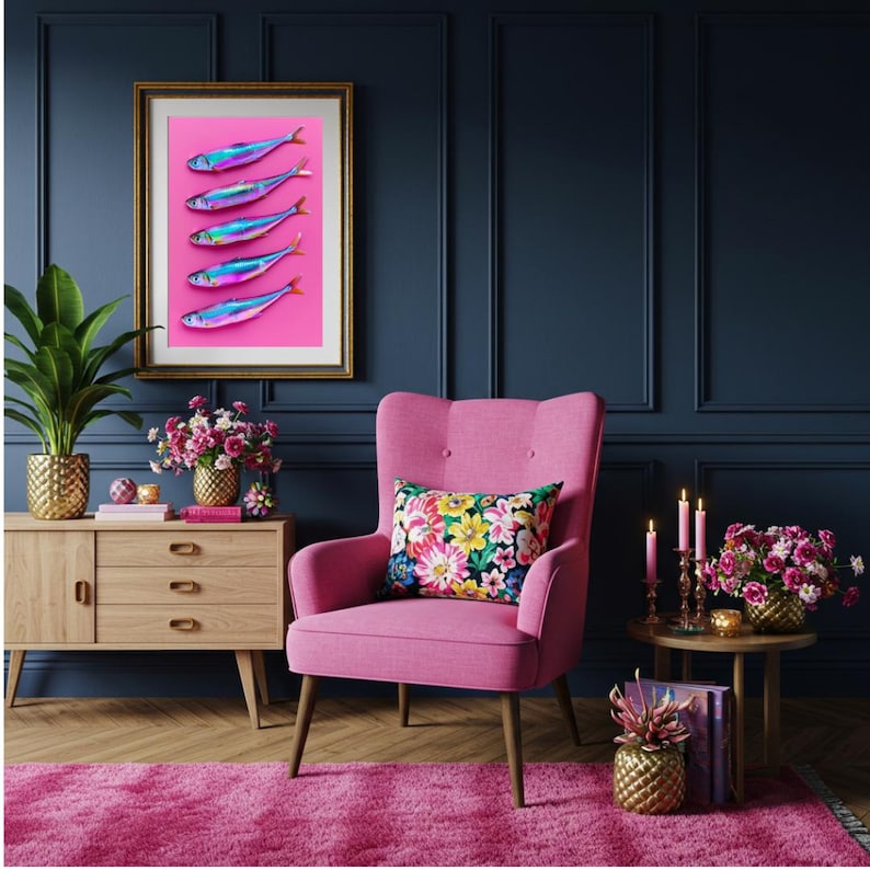 May include: A framed art print featuring five iridescent fish on a pink background. The artwork hangs above a pink armchair with a floral pillow. The room has a dark blue wall, a wooden cabinet, and a pink rug.