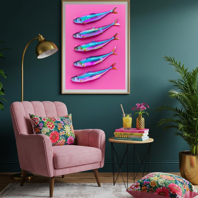 May include: A framed art print featuring five iridescent fish arranged vertically on a vibrant pink background. The fish have blue, purple, and silver hues with orange tail fins. The artwork is displayed in a room with a pink armchair and floral pillow.
