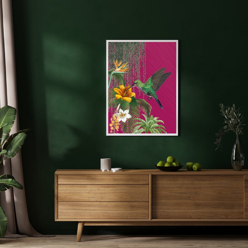 K&ouml;nnte beinhalten: Ein gerahmter Druck eines Kolibris im Flug, mit gr&uuml;nen und braunen Federn, der in der N&auml;he einer gelben Blume mit gr&uuml;nen Bl&auml;ttern schwebt. Der Hintergrund ist leuchtend pink.