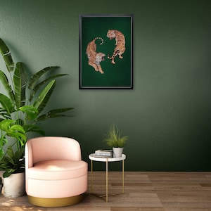 Op de afbeelding: Een ingelijst afdruk van twee tijgers op een groene achtergrond. De tijgers staan ​​tegenover elkaar met hun staarten in elkaar gevlochten. De afdruk hangt aan een groene muur.