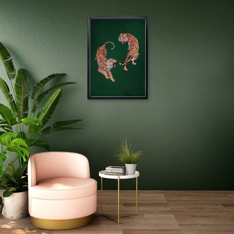 Op de afbeelding: Een ingelijst afdruk van twee tijgers op een groene achtergrond. De tijgers staan ​​tegenover elkaar met hun staarten in elkaar gevlochten. De afdruk hangt aan een groene muur.