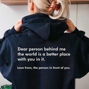 Op de afbeelding: Zwart hoodie met witte tekst die luidt: "Lieve persoon achter me, de wereld is een betere plek met jou erin. Liefs van de persoon voor je."