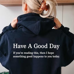 以下が含まれることがあります： 黒いフード付きスウェットシャツに、白い文字で「Have A Good Day. If you're reading this, then I hope something good happens to you today.」と書かれています。