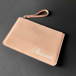 Op de afbeelding: Een lichtroze clutch met een polsbandje en de naam "Shaema" geborduurd in wit.