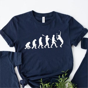 Puede incluir: Una camiseta azul marino con un gráfico blanco de la evolución del hombre, que termina con un hombre jugando al tenis.