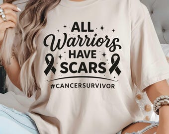 May include: A beige t-shirt with the text "ALL Warriors HAVE SCARS" in black script and a black ribbon graphic. The hashtag "#CANCERSURVIVOR" is printed below the text. The shirt is a casual style.