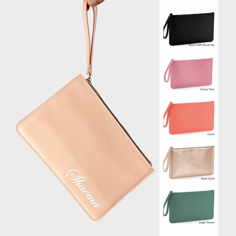 Op de afbeelding: Een blush roze clutch met een witte gepersonaliseerde inscriptie die "Shaema" luidt. De tas heeft een ritssluiting bovenaan en een polsbandje.