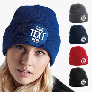 Può includere: Cinque berretti di lana di diversi colori con una toppa circolare bianca che dice "YOUR TEXT HERE" in lettere bianche.