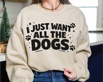 May include: A beige sweatshirt with the text "I JUST WANT ALL THE DOGS" in black. The design includes paw prints and stars. The sweatshirt is a casual style, suitable for dog lovers.