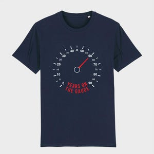May include: Dark navy blue t-shirt with a speedometer graphic. The gauge reads 60, with the text "YEARS ON THE GAUGE" in red. A novelty t-shirt, perfect for a birthday or special event.