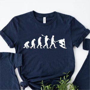 May include: A navy blue t-shirt with a white graphic of the evolution of man, ending with a surfer riding a wave.