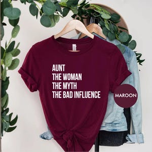 Pode incluir: Camiseta de cor vinho com texto branco que diz "Aunt The Woman The Myth The Bad Influence".