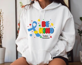 May include: White hoodie with a colorful graphic that reads "BE KIND" with a blue ribbon and puzzle pieces. The text "Autism Awareness" is below the main text. The hoodie has a front pocket and a hood.