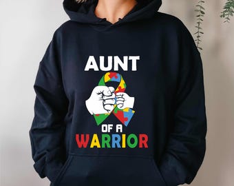 May include: Navy blue hoodie with the text "AUNT OF A WARRIOR" in white and rainbow colors. The design features two white fists holding a colorful puzzle ribbon, symbolizing autism awareness. A comfortable and stylish sweatshirt.