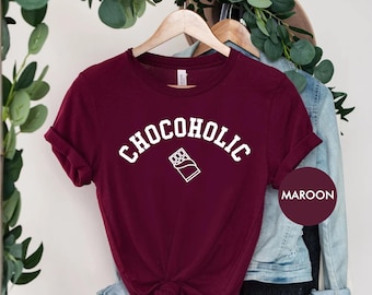 Peut inclure: Un t-shirt marron avec le texte "CHOCOholic" en blanc, avec un contour blanc d'une barre de chocolat en dessous.