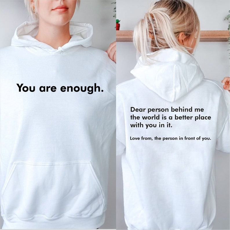 May include: White hoodie with the text "You are enough." on the front and the text "Dear person behind me the world is a better place with you in it. Love from, the person in front of you." on the back.