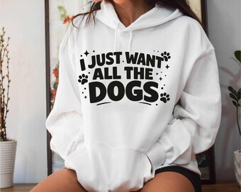May include: White hoodie with the text "I JUST WANT ALL THE DOGS" in black. The design includes paw prints and stars. The hoodie has a front pocket and a hood.