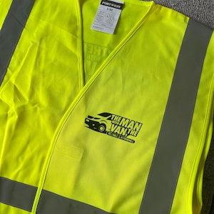 K&ouml;nnte beinhalten: Eine leuchtend gelbe Sicherheitsweste mit reflektierenden silbernen Streifen. Die Weste hat ein schwarzes Logo mit der Aufschrift "The Man With The Van" und den Text "Reliable & Affordable".