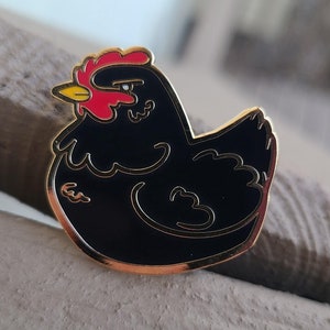May include: Black enamel pin of a chicken with a red comb and wattle. The chicken is facing left and has a gold outline.