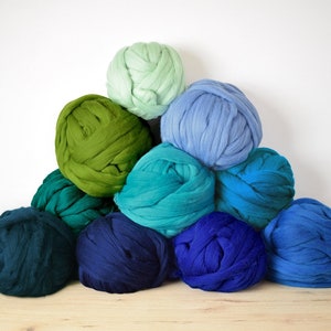 May include: A pile of colorful yarn balls in shades of green, blue, and teal. The yarn is arranged in a pyramid shape, with the lightest color at the top and the darkest color at the bottom.