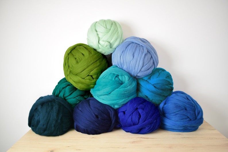 May include: A pile of colorful yarn balls in shades of green, blue, and teal. The yarn is arranged in a pyramid shape, with the lightest color at the top and the darkest color at the bottom.