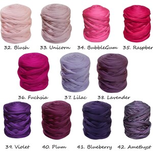 May include: Twelve skeins of yarn in various shades of pink, purple, and blue. The yarn is arranged in four rows of three skeins each. The skeins are labeled with numbers and names, such as "Blush", "Unicorn", "BubbleGum", "Raspberry", "Fuchsia", "Lilac", "Lavender", "Violet", "Plum", "Blueberry", and "Amethyst".