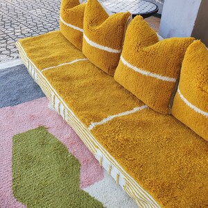 May include: A yellow tufted couch with white stripes and four matching pillows. The couch is on a multi-colored rug with pink, green, and gray sections.