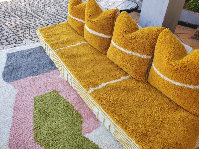 May include: A yellow tufted couch with white stripes and four matching pillows. The couch is on a multi-colored rug with pink, green, and gray sections.