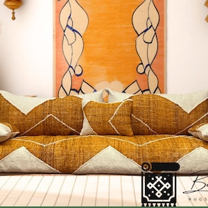 Puede incluir: Un cojín de suelo amarillo mostaza y blanco con un patrón geométrico. El cojín está hecho de tejido tejido y tiene una sensación cómoda y firme. Es perfecto para crear una zona de estar acogedora y atractiva en tu hogar.