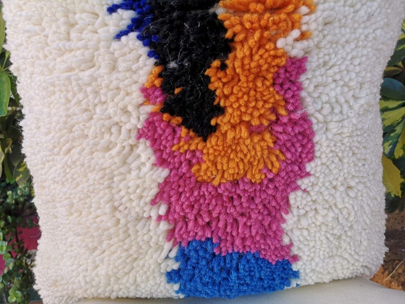 May include: A white throw pillow with a colorful abstract design. The design features orange, pink, blue, and black colors in a geometric pattern.