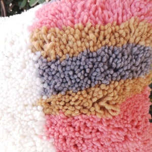 May include: A close-up of a colorful, fluffy rug with stripes of white, pink, gray, and brown. The rug is made of a soft, textured material.