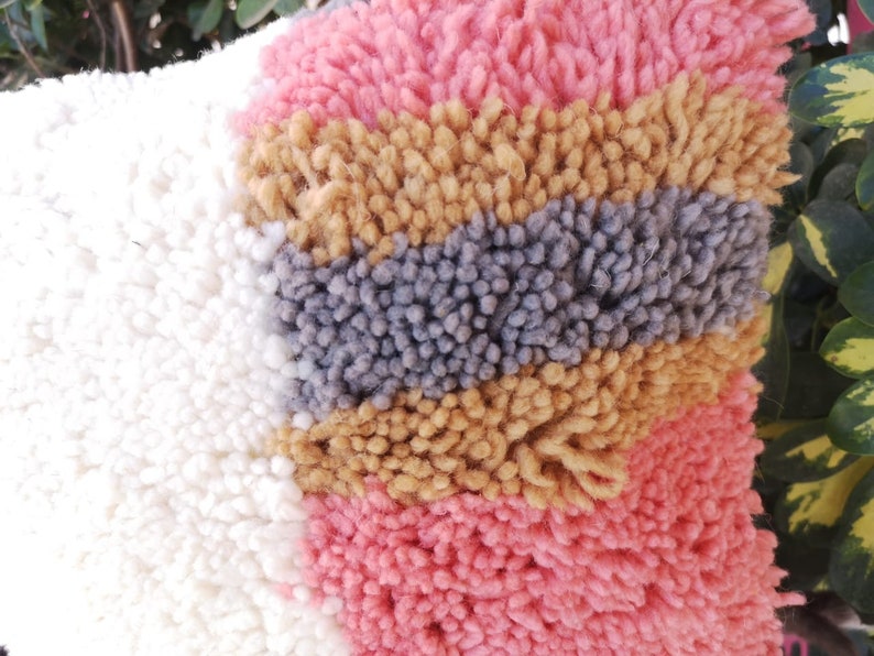 May include: A close-up of a colorful, fluffy rug with stripes of white, pink, gray, and brown. The rug is made of a soft, textured material.