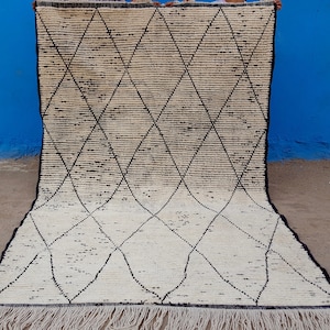 Puede incluir: Una alfombra marroqu&iacute; blanca y negra con un patr&oacute;n de diamantes. La alfombra tiene un borde de flecos.