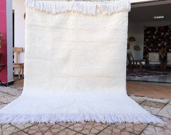 May include: A white shag rug with a fringe border. The rug is laid out on a tiled floor.