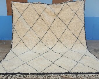 May include: A white Moroccan rug with a black diamond pattern. The rug has a fringe border.