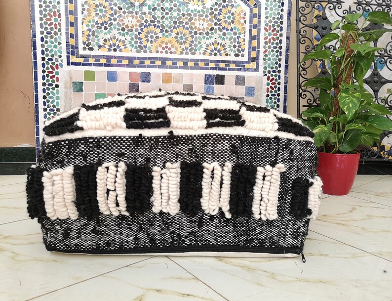 May include: Black and white woven pouf with a geometric pattern. The pouf has a zipper on the side and is made of a soft, fluffy material.