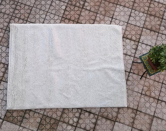 May include: A white fluffy rug with a textured surface. The rug is laid out on a tiled floor with a geometric pattern.