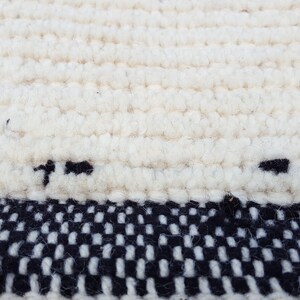 Puede incluir: Una alfombra blanca tejida con un borde a cuadros blanco y negro. La alfombra est&aacute; hecha de un material suave y esponjoso.