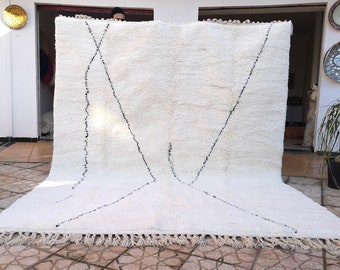 May include: A white Moroccan rug with a black geometric design. The rug has a fringe border and is made of wool.