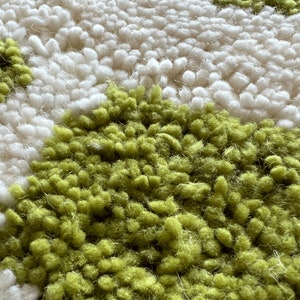 May include: Close-up of a white and green rug with a textured, fluffy surface. The rug has a pattern of small, round shapes.