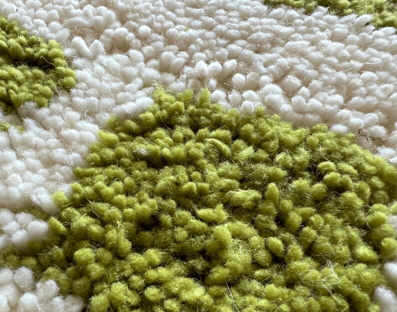 May include: Close-up of a white and green rug with a textured, fluffy surface. The rug has a pattern of small, round shapes.