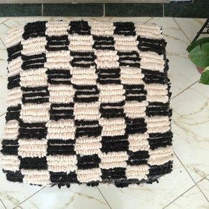 May include: Black and white checkered floor cushion made of fluffy yarn.