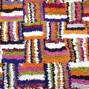 May include: A colorful rug with a geometric pattern of squares and rectangles. The rug is made of thick, textured yarn in shades of orange, pink, green, blue, white, and black.