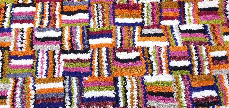 May include: A colorful rug with a geometric pattern of squares and rectangles. The rug is made of thick, textured yarn in shades of orange, pink, green, blue, white, and black.