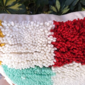 May include: A colorful throw pillow with a geometric pattern. The pillow is made of a soft, textured fabric and features a variety of colors, including yellow, white, red, and green.