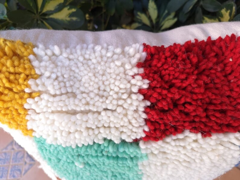 May include: A colorful throw pillow with a geometric pattern. The pillow is made of a soft, textured fabric and features a variety of colors, including yellow, white, red, and green.