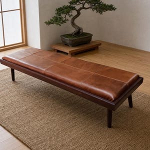 May include: A rectangular bench featuring a dark brown wooden frame and a smooth, tan leather seat cushion divided into six square sections. The bench is supported by four tapered wooden legs and has a low-profile design with clean lines.