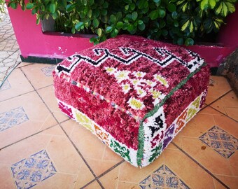 Puede incluir: Un puf cuadrado de color rojo, blanco y verde con una textura esponjosa. El puf está hecho de tejido tejido.